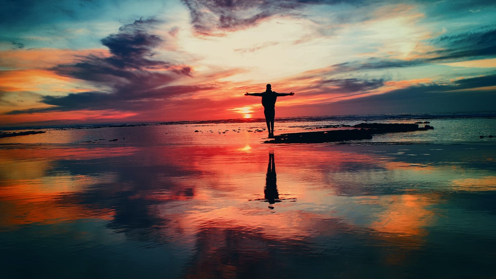 silhouette of person standing on rock surrounded by body of water