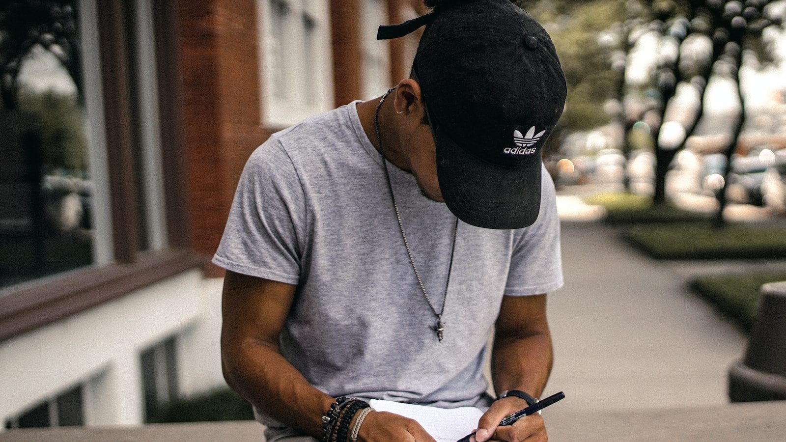 person in black adidas cap sitting on bench writing on notebook