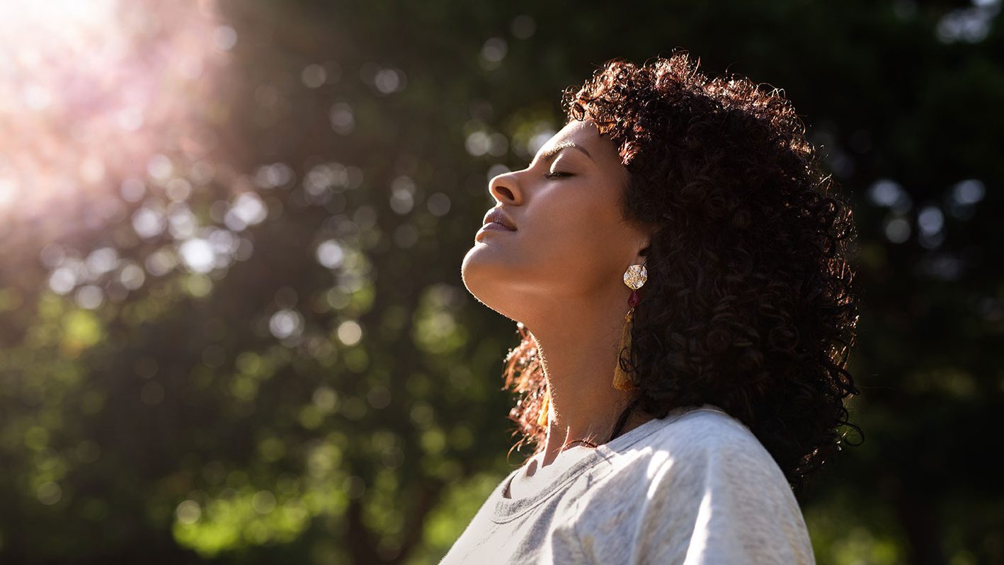 Woman breathes deeply in sunny park