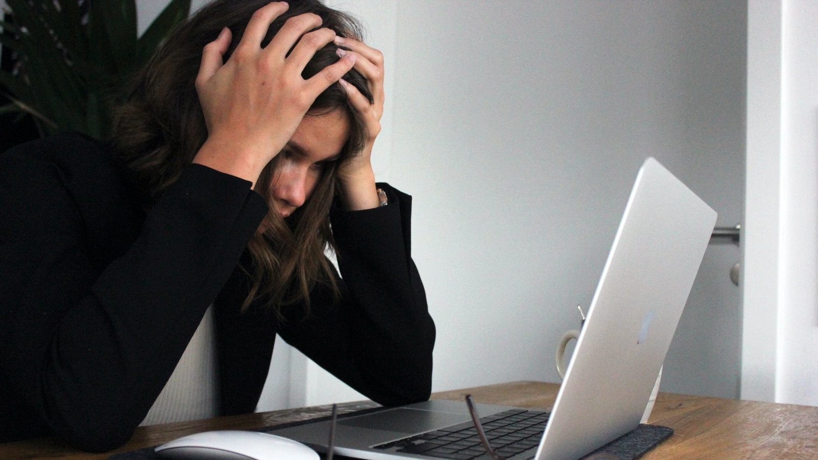 burnout; woman in black long sleeves holds head in hands while staring at laptop