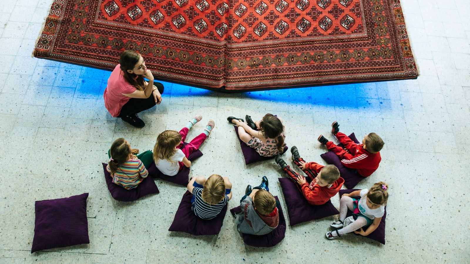 children and woman sitting on floor with pillows