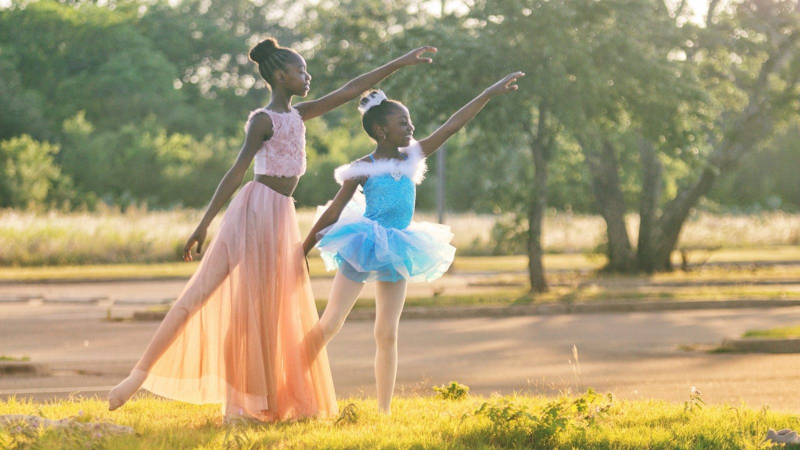 two girls wearing blue and peach dresses dancing on green grass