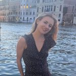 Michal Miller wears a black dress and stands in front of a canal in Italy
