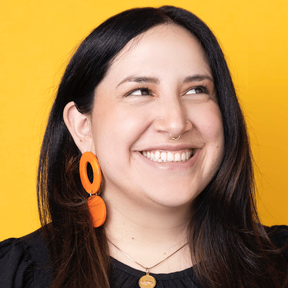 Pame Barba has brown hair and stands against an orange background