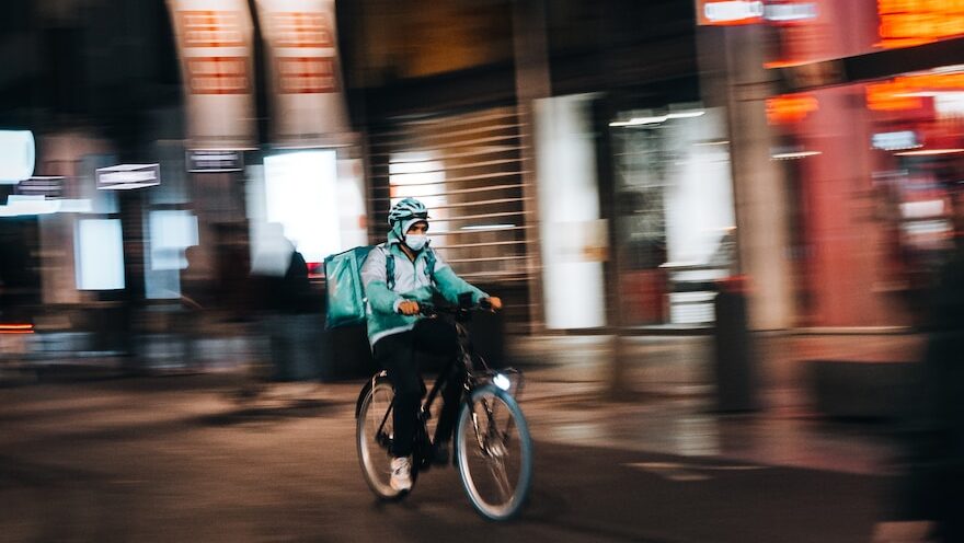 Gig workers include contract workers like food delivery workers and Uber drivers. Image description: a man riding a motorcycle down a street at night