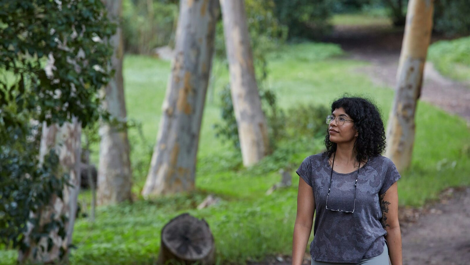 Ecological well-being describes the interconnected relationship between human and planetary health. The image depicts a woman with curly black hair walking and glasses, walking down a path in the woods