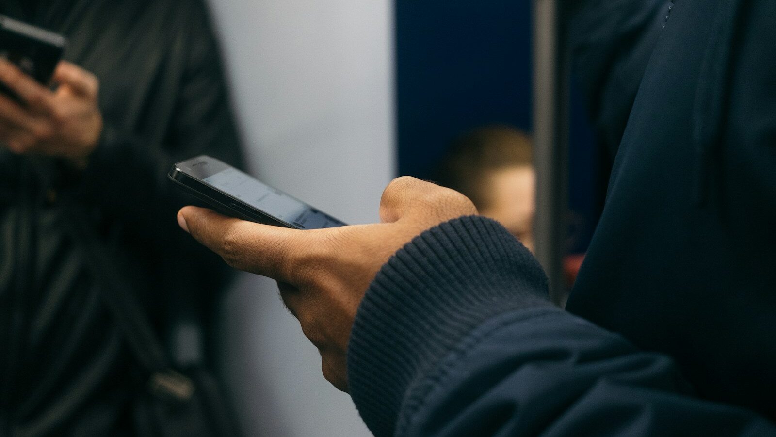 Two men on public transit using smart phones. Digital spaces like social media, news apps, and online games shape an individual's sense of self and social interactions.