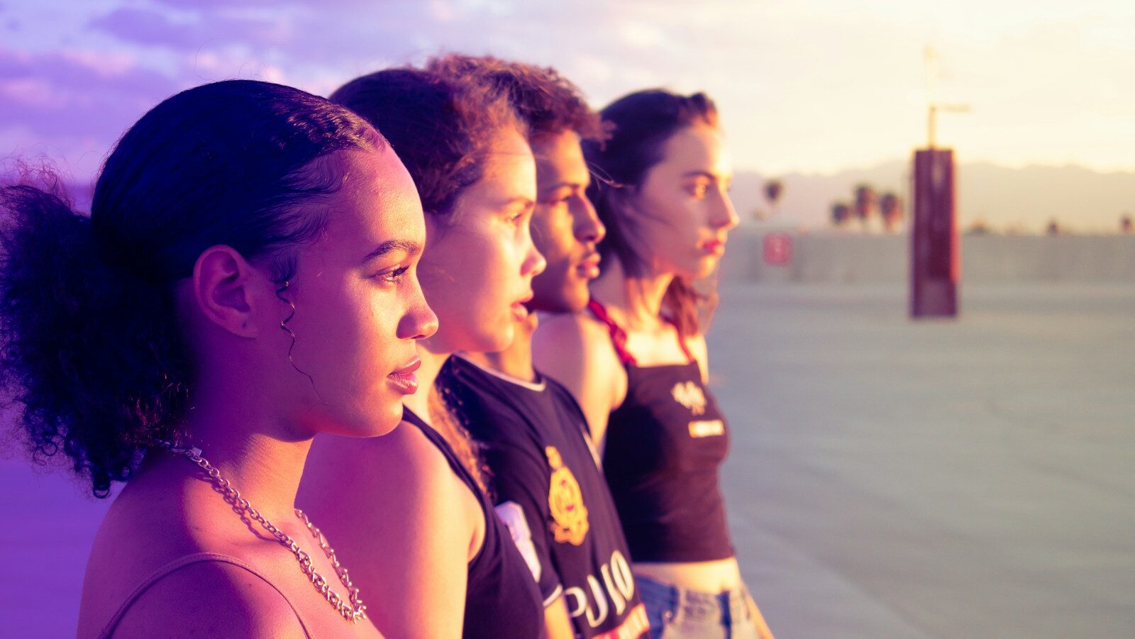 Community coaching. Four teenagers stand on a beach facing the sunset