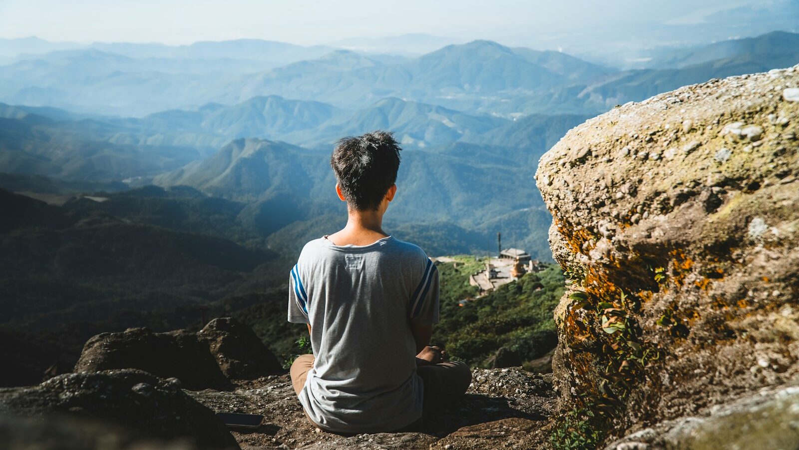 a man sitting on top of a mountain, meditation and other spiritual practices help individual's find inner peace, or the resilience to navigate challenges and uncertainty