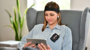 a woman sitting in a chair using a tablet. Technologies like wearable neurofeedback monitors signal possible futures where brain monitoring informs coaching.