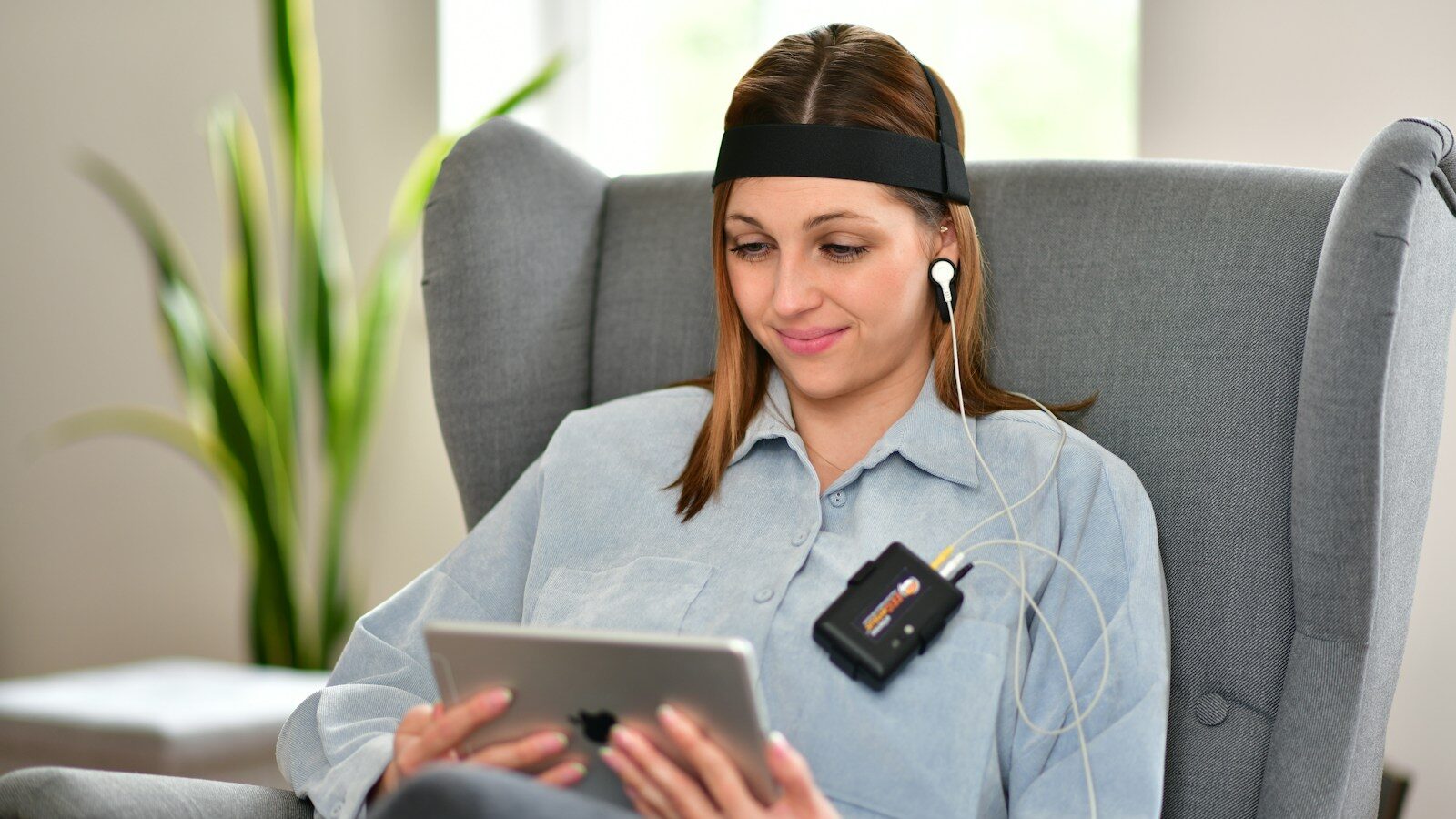 a woman sitting in a chair using a tablet. Technologies like wearable neurofeedback monitors signal possible futures where brain monitoring informs coaching.